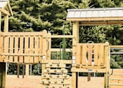 Thumbnail 13 of 15 - A wooden playground with a green slide and a yellow slide.