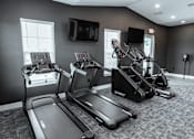Thumbnail 18 of 29 - A gym with treadmills, elliptical machines, and a television.
