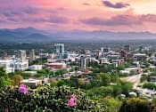 Thumbnail 14 of 15 - A cityscape with buildings and a mountain range in the background.
