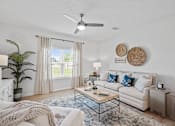 Thumbnail 9 of 15 - A living room with a white couch, a coffee table, and a ceiling fan.