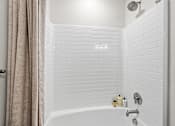 Thumbnail 21 of 39 - A white tiled bathroom with a shower and a white bathtub.