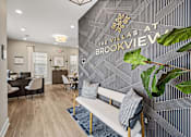 Thumbnail 28 of 39 - A living room with a couch and a plant in front of a wall with a sign that says "Villas at Brookview".