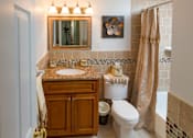 Thumbnail 8 of 13 - A bathroom with a brown cabinet, a white toilet, and a brown shower curtain.