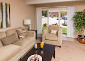 Thumbnail 4 of 13 - A living room with a beige couch, a chair, a table with a candle, and a painting on the wall.