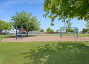Thumbnail 8 of 13 - Belaire's playground area includes monkey bars and a swing set. It is surrounded by a grassy field area and a number of trees.