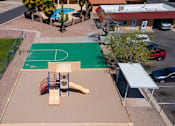 Thumbnail 8 of 10 - A basketball court is surrounded by a green fence and a playground.
