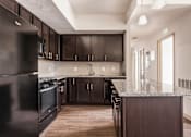 Thumbnail 14 of 16 - A kitchen with dark wood cabinets and a black refrigerator.