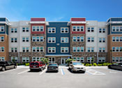 Thumbnail 13 of 14 - A parking lot with cars and a multi-story building with red, white, and blue sections.