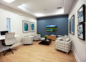 Thumbnail 9 of 14 - A room with a desk, chairs, and a television.