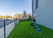 Thumbnail 9 of 9 - A grassy area with a bench and a fence in front of a building.