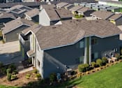 Thumbnail 3 of 15 - A large grey house with a brown roof and a green lawn in front.