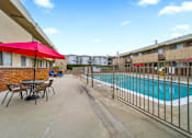 Thumbnail 14 of 14 - A pool area with a table and chairs and a red umbrella.