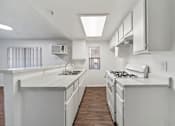 Thumbnail 7 of 10 - A white kitchen with a stove top oven and a sink.