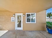Thumbnail 4 of 9 - A beige building with a white door and a sign on the wall.