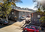 Thumbnail 1 of 5 - A red car is parked in front of a building with a black fence.