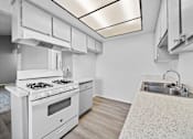 Thumbnail 14 of 20 - A white kitchen with a stove, sink, and cabinets.