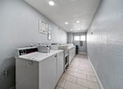 Thumbnail 4 of 9 - A clean, white-walled industrial kitchen with a row of white ovens and a white countertop.