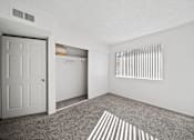 Thumbnail 11 of 13 - A room with a white door, a window with blinds, and a closet with clothes.