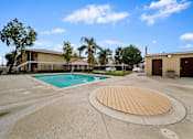 Thumbnail 6 of 8 - A large outdoor swimming pool with a wooden deck in the middle of a concrete area.