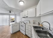 Thumbnail 12 of 20 - A white kitchen with a stove, sink, and fan.
