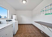 Thumbnail 15 of 20 - A white washing machine sits in a room with a window and a tiled floor.