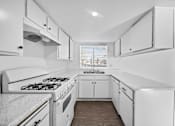 Thumbnail 10 of 12 - A white kitchen with a stove and cabinets.