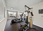 Thumbnail 6 of 8 - A gym with a rowing machine, a stationary bike, and a weight machine.