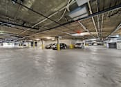 Thumbnail 3 of 10 - A parking garage with concrete floors and yellow poles.