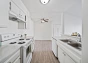 Thumbnail 9 of 13 - A white kitchen with a stove, sink, and cabinets.