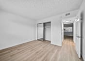 Thumbnail 7 of 16 - A room with white walls and wood flooring, with a doorway leading to another room.