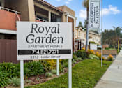 Thumbnail 2 of 16 - A sign for Royal Garden Apartment Homes stands in front of a building.