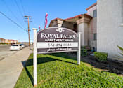 Thumbnail 5 of 10 - A sign for Royal Palms Apartment Homes stands in front of a building.