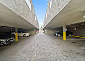 Thumbnail 1 of 8 - A parking garage with cars parked on both sides of the aisle.