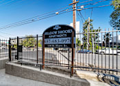 Thumbnail 4 of 10 - A sign for Shadowbrooks Apartments is displayed in front of a fence.