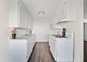 Thumbnail 8 of 11 - A white kitchen with a sink, stove, and cabinets.
