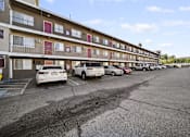 Thumbnail 1 of 11 - A parking lot in front of a multi-story apartment building with cars parked.
