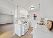 Thumbnail 7 of 16 - A white kitchen with a stove, sink, and cabinets.