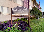 Thumbnail 1 of 8 - A sign for South Oaks Pointe Apartments stands in front of a building.