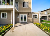 Thumbnail 2 of 9 - A building with a white door and windows with flower beds in front.
