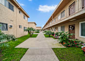 Thumbnail 4 of 15 - A concrete walkway leads between two rows of apartment buildings.
