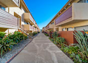 Thumbnail 2 of 9 - A concrete pathway leads through a row of modern apartment buildings.
