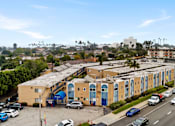 Thumbnail 6 of 12 - A parking lot with cars and a yellow building with blue doors.