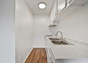 Thumbnail 12 of 12 - A small, white kitchen with a sink and a wood floor.