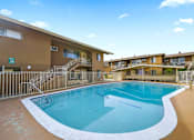 Thumbnail 11 of 13 - A large outdoor swimming pool surrounded by a fence and buildings.