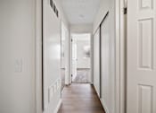 Thumbnail 6 of 14 - A long hallway with white walls and wood floors.