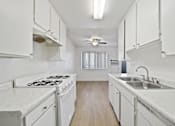 Thumbnail 12 of 14 - A white kitchen with a stove, sink, and cabinets.