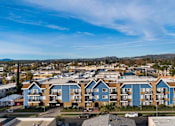 Thumbnail 10 of 14 - Apartment complex with blue and beige buildings under a clear sky.