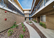 Thumbnail 4 of 14 - A concrete pathway leads through a landscaped courtyard between two apartment buildings.