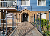 Thumbnail 2 of 14 - A blue building with a black gate and a wooden walkway leading to a tunnel entrance.
