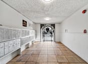 Thumbnail 11 of 14 - A long hallway with a metal gate at the end and mailboxes on the left.